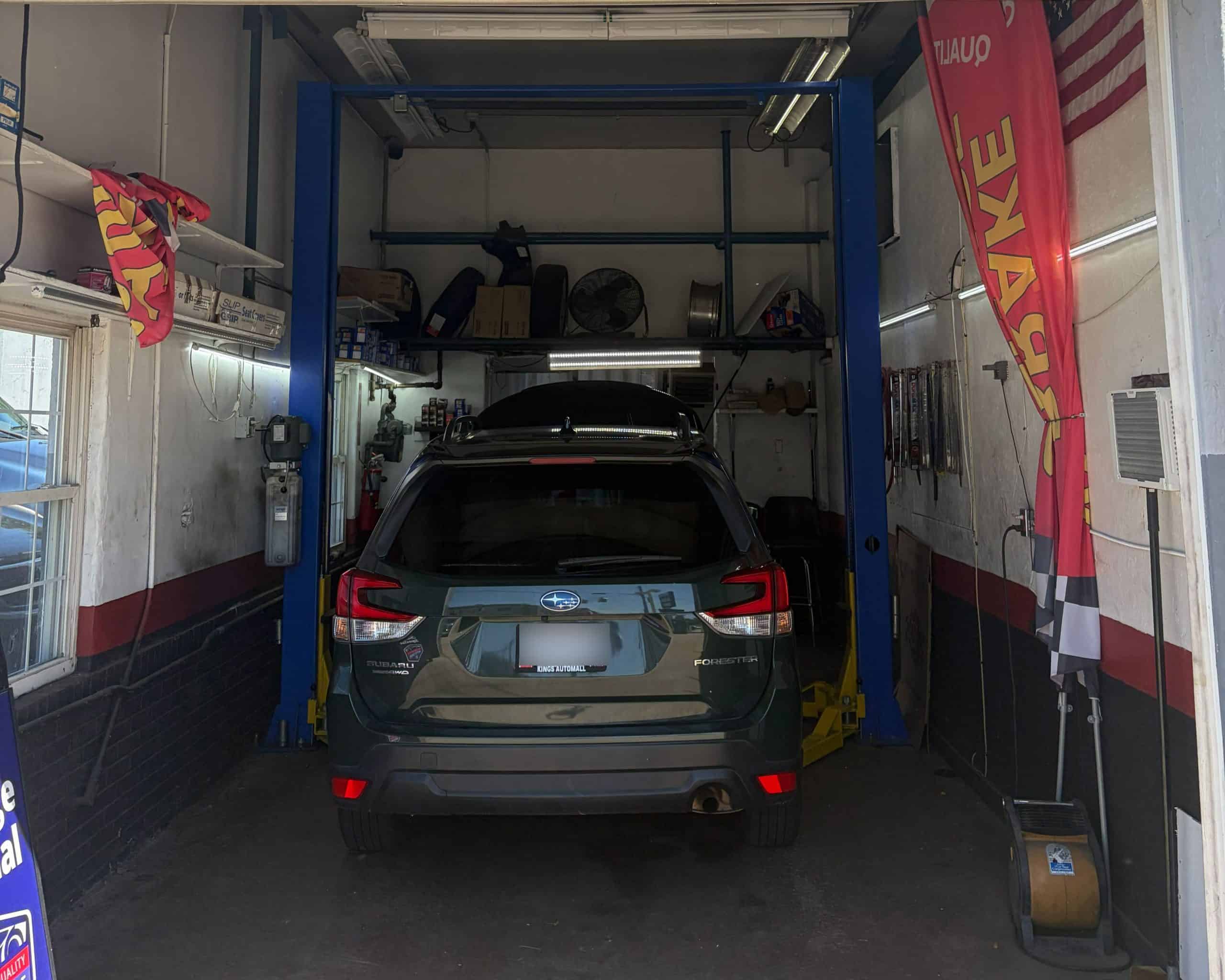 Black SUV in auto repair shop with lift and tools.