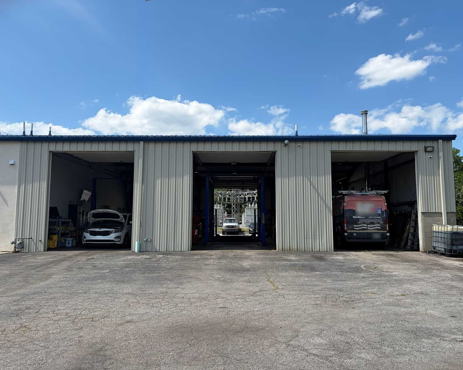 Auto repair shop with three bays and vehicles inside under a blue sky.
