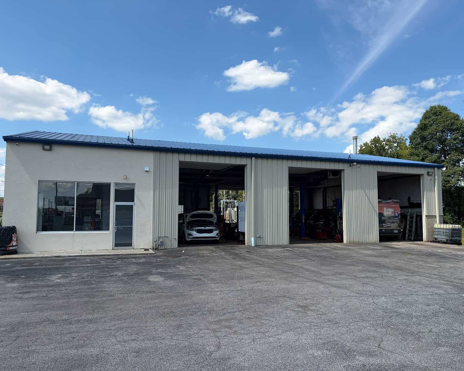 Auto repair shop with open bays and cars inside under a blue sky.