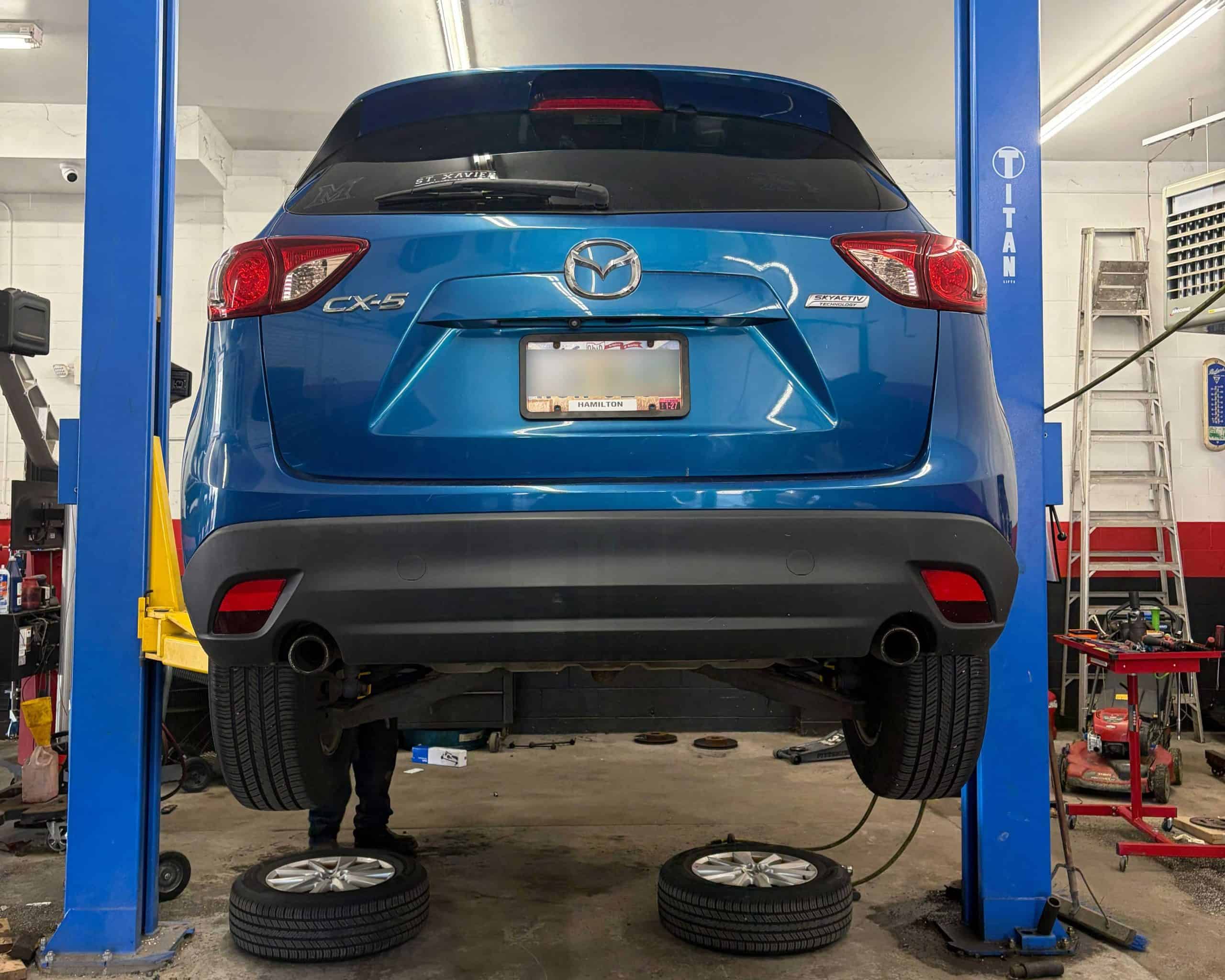 Blue Mazda CX-5 vehicle lifted for maintenance at auto repair shop.
