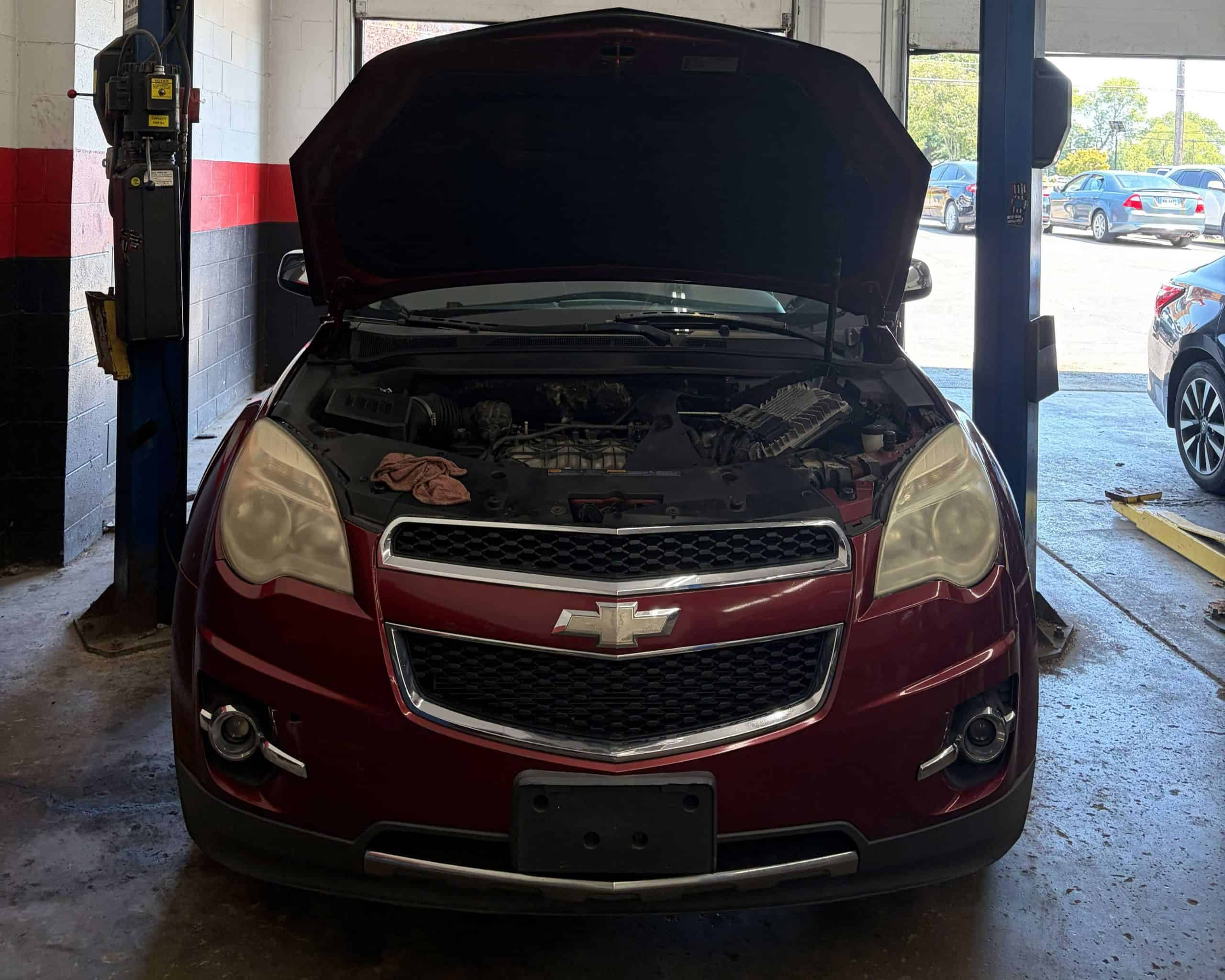 Red Chevrolet car with open hood at auto repair shop in Delhi.