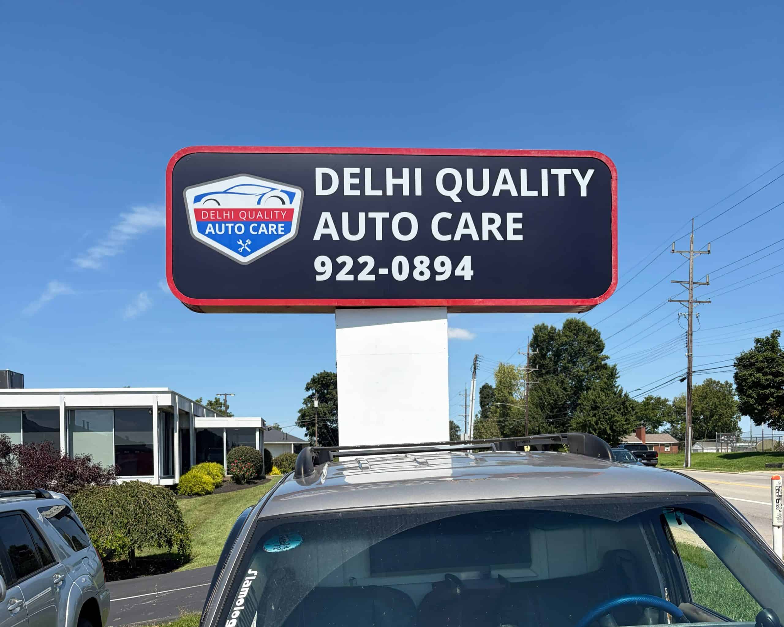 Delhi Quality Auto Care signboard with contact number on clear day.